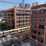 view of sky, workbox river north building roof and train traveling over a bridge over a street