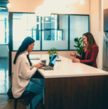 Two women sit at a table with a laptop in the West Loop office.